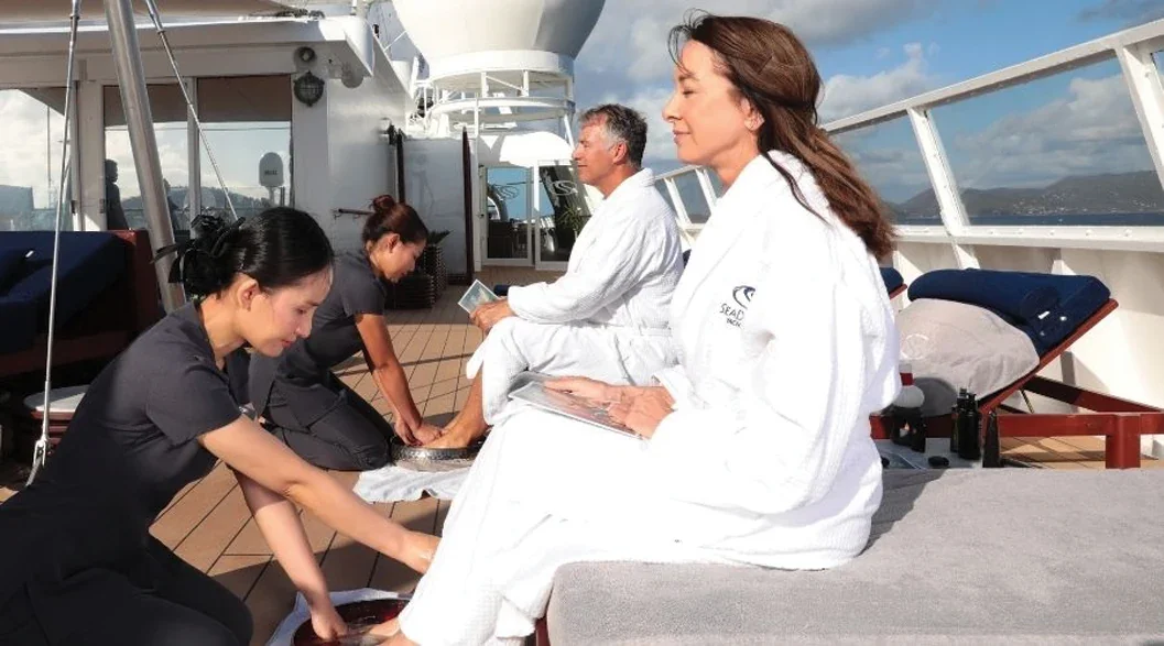 Guests enjoying a relaxing foot-bath spa treatment on the open deck of a SeaDream yacht while navigating scenic coastal waters.