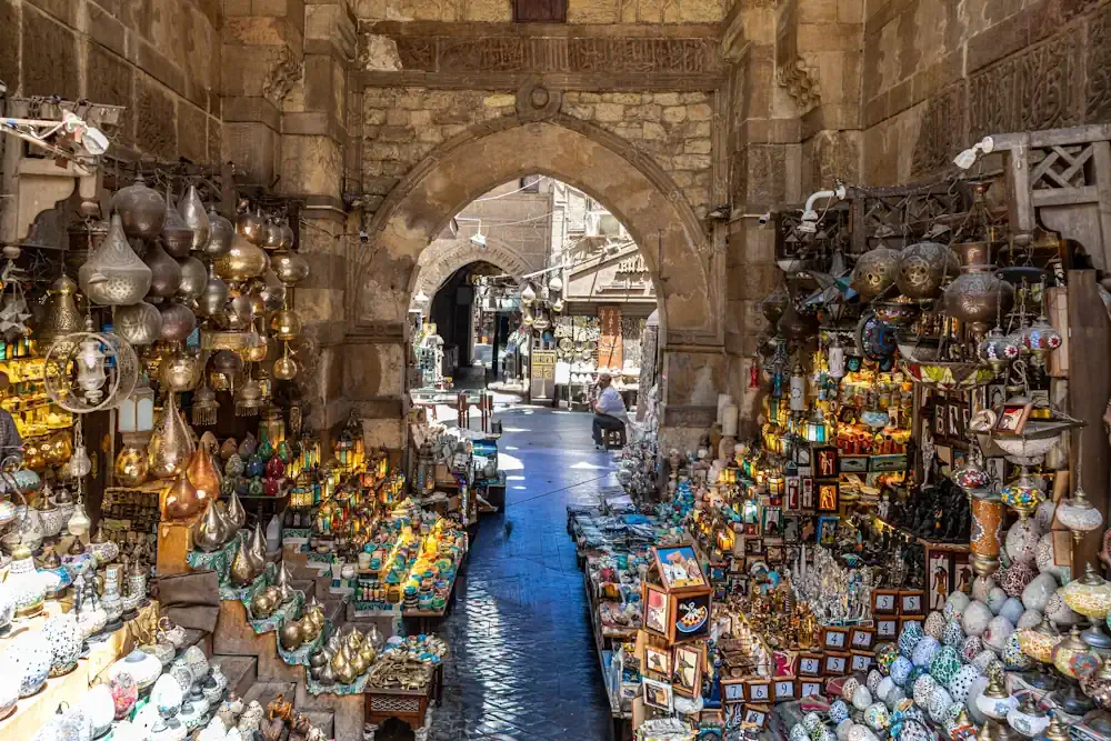 Glimmering handcrafted brass lanterns and mosaic glass lamps filling a historic stone archway inside Khan El-Khalili Bazaar in Cairo, Egypt.