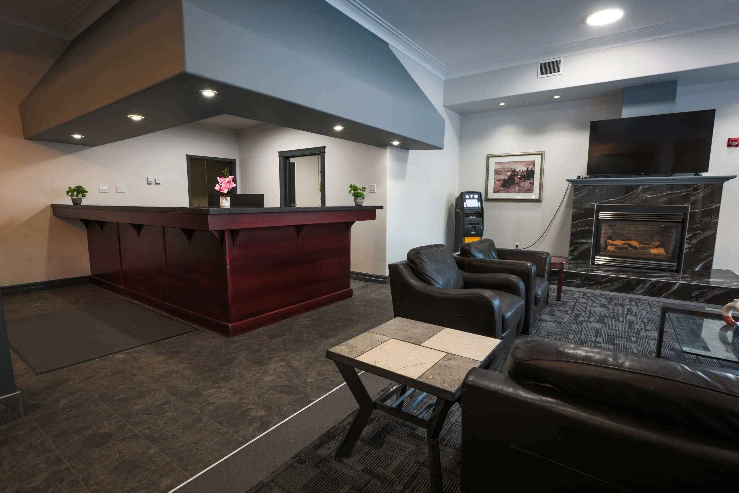 Lobby with black leather chairs, a marble fireplace, a framed picture on the wall, a TV, a small table, and playing area with tile and carpeted flooring.