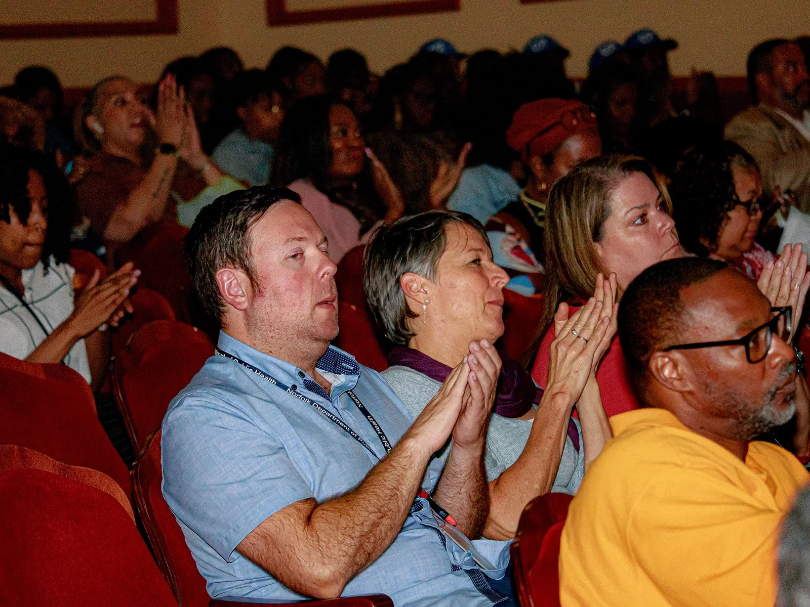 Audience members sitting in theater seats, applauding and watching a presentation or performance.