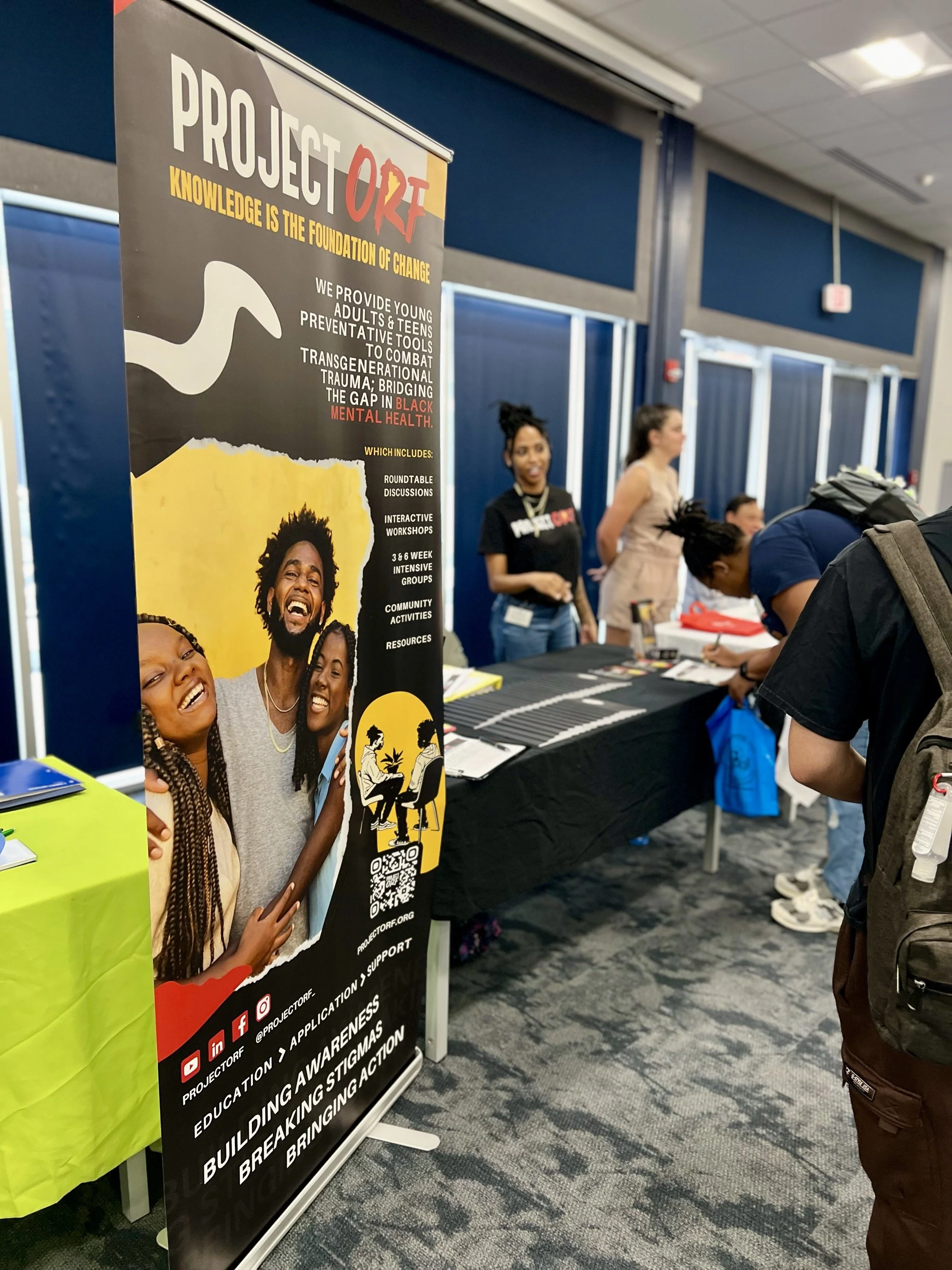 A promotional banner for Project ORF with a group of diverse smiling people, likely at an informational booth or event, in a room with other people and tables.