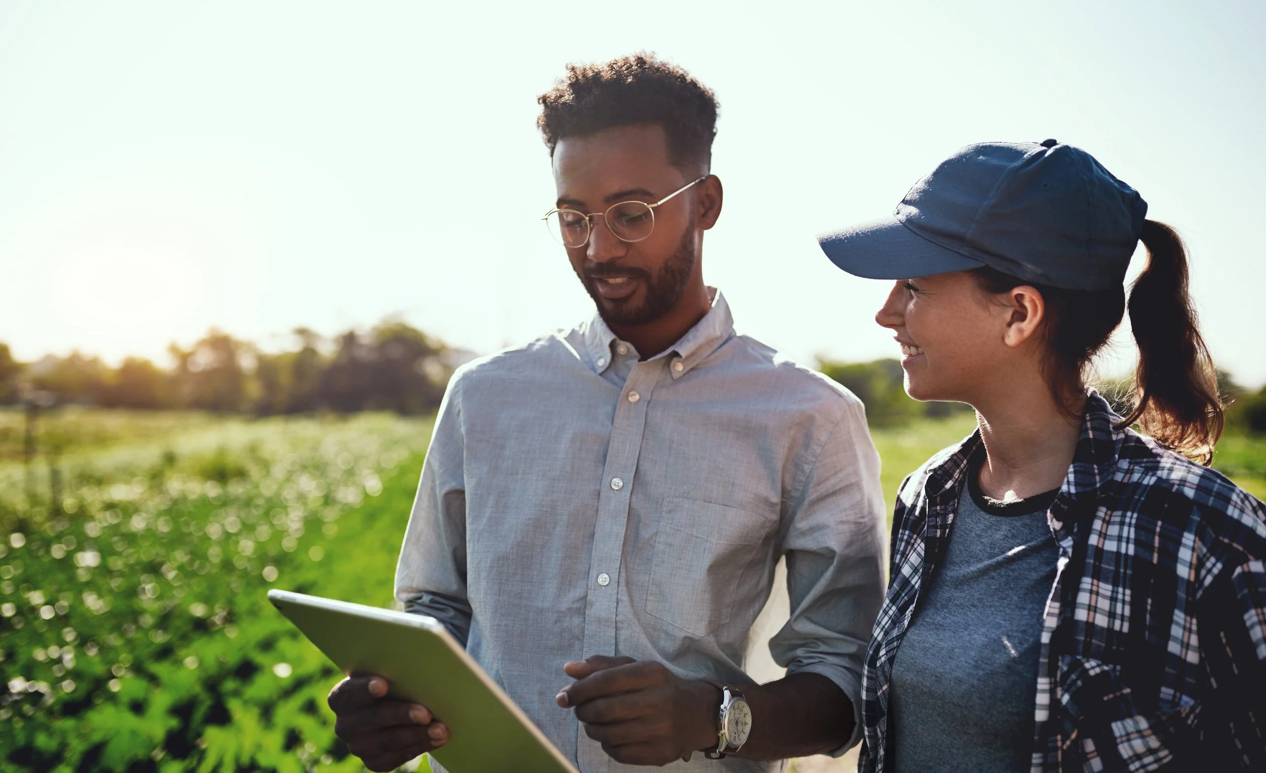 Two farmers, a man and a woman, looking at a tablet in a field during daylight.