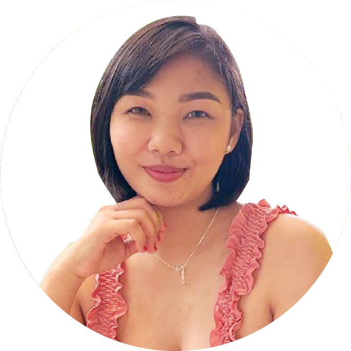 A woman with short black hair wearing a coral ruffled top and a necklace, smiling at the camera.