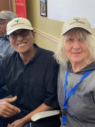 Two women smiling for a photo, wearing caps with a logo, standing close together indoors.