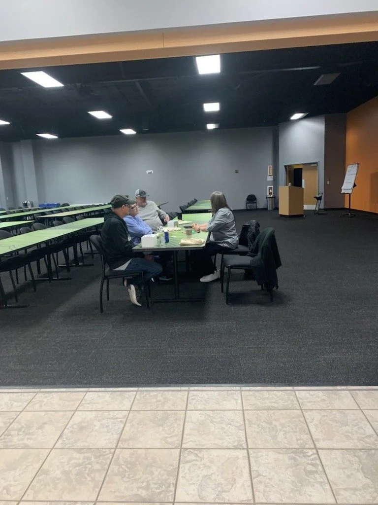 Four people sitting and talking around a table in a large, empty conference room with green tables and a black ceiling.