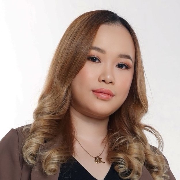 Portrait of a woman with wavy, shoulder-length hair, wearing makeup and a necklace, against a plain white background.