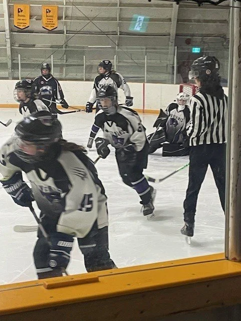 Ice hockey players in black and white jerseys and a referee in black and white stripes on the ice rink during a game.