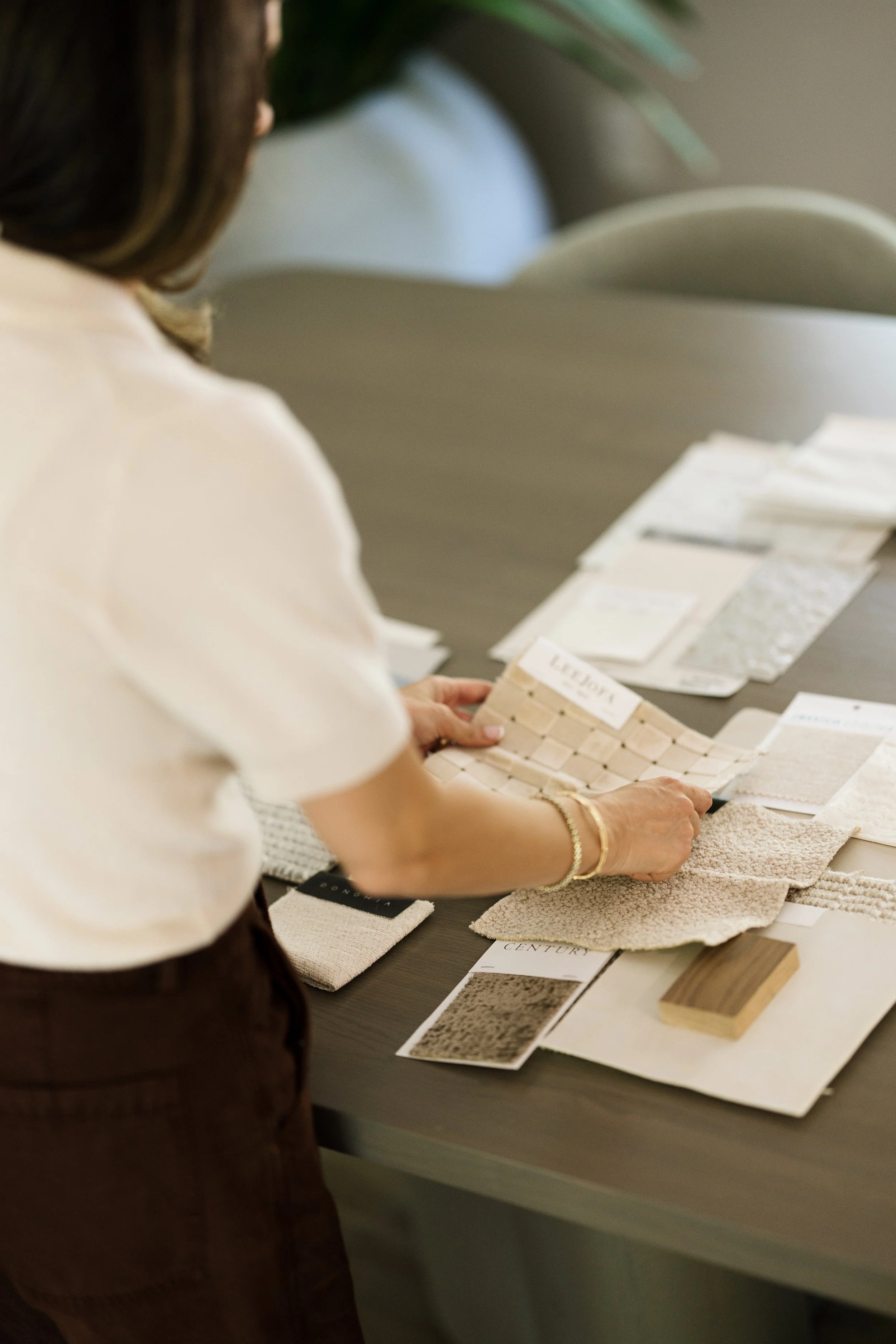 A woman looking at fabric samples and color swatches on a table, with various fabric swatches, color cards, and textured material samples spread out.
