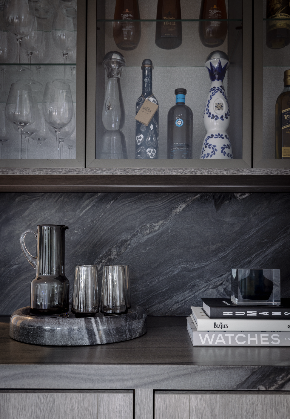 A kitchen or bar area with glassware, liquor bottles, and decorative items on a dark stone countertop and shelf.