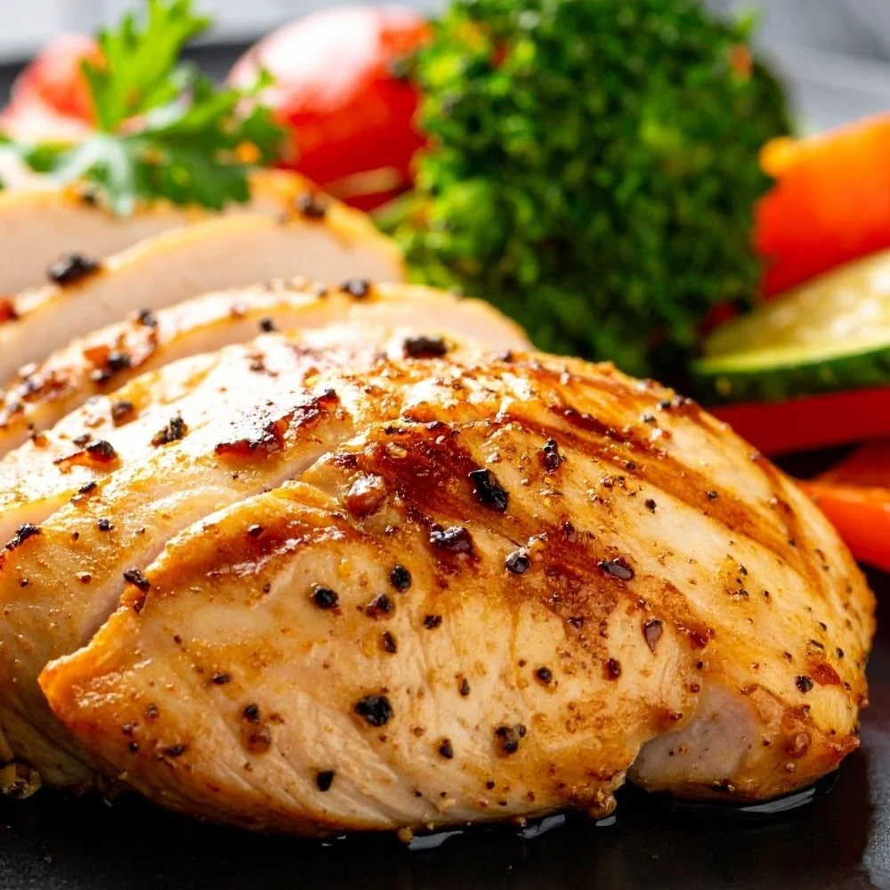 Cooked, seasoned chicken breast with herbs and black pepper, served with fresh vegetables including tomato, cucumber, and broccoli.