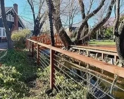 A wooden fence along a canal or stream with trees and houses in the background.