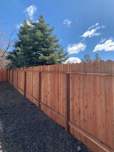A wooden privacy fence with a tree and blue sky with clouds in the background.