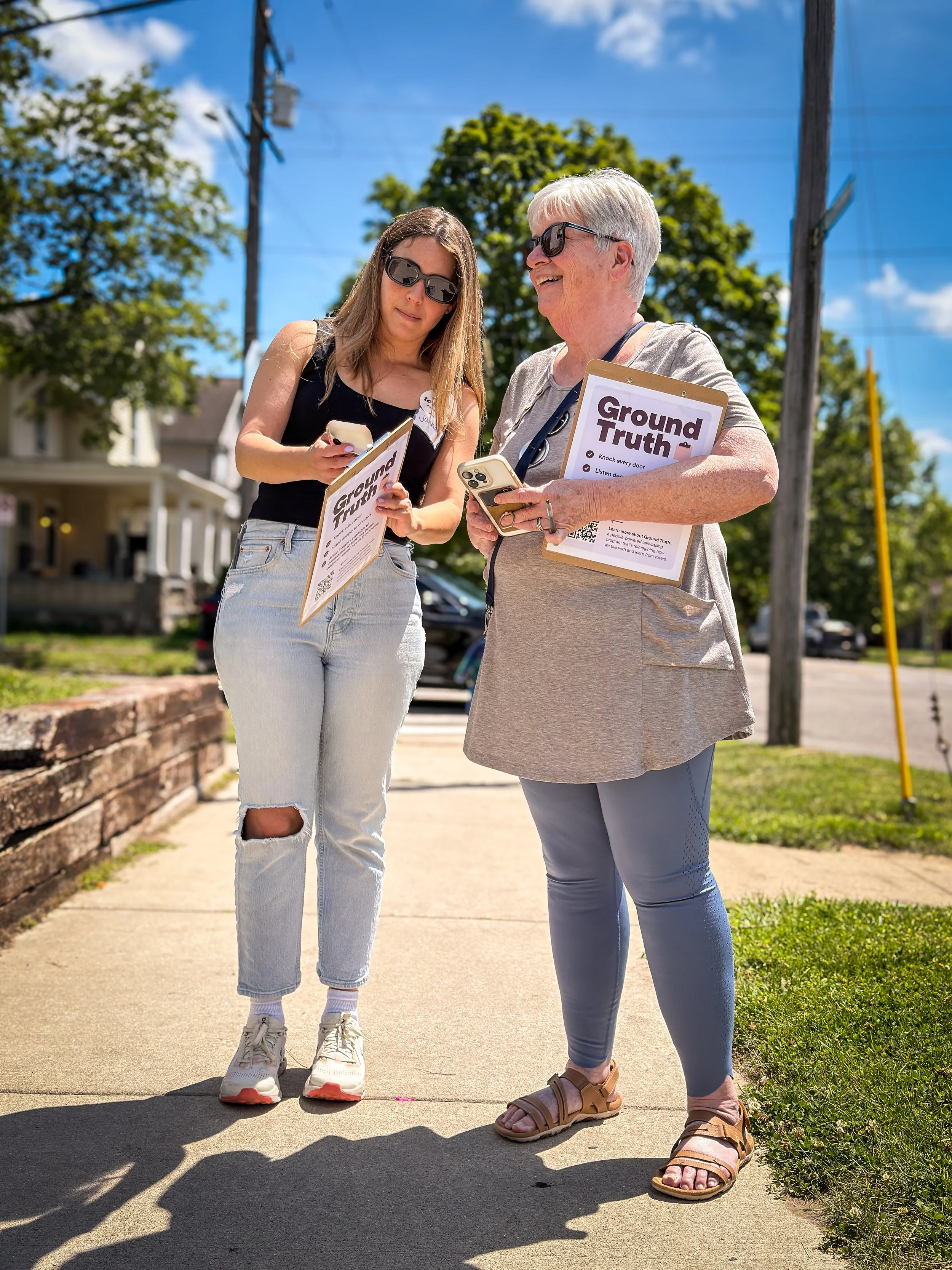 Ground Truth volunteers holding clip boards and using their cell phones while canvassing on a bright, sunny day.