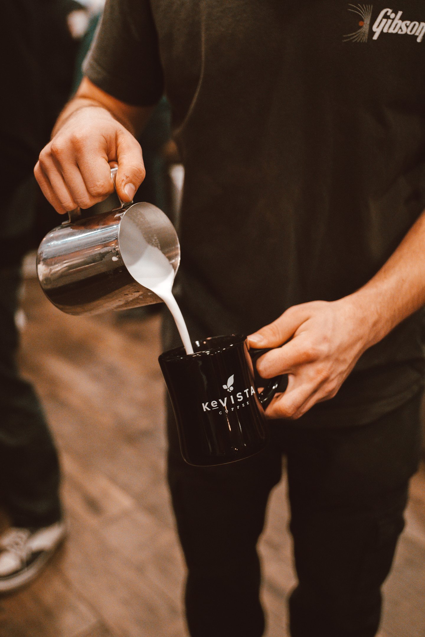 Two people in a coffee shop, one preparing a drink at an espresso machine, the other in the background observing.