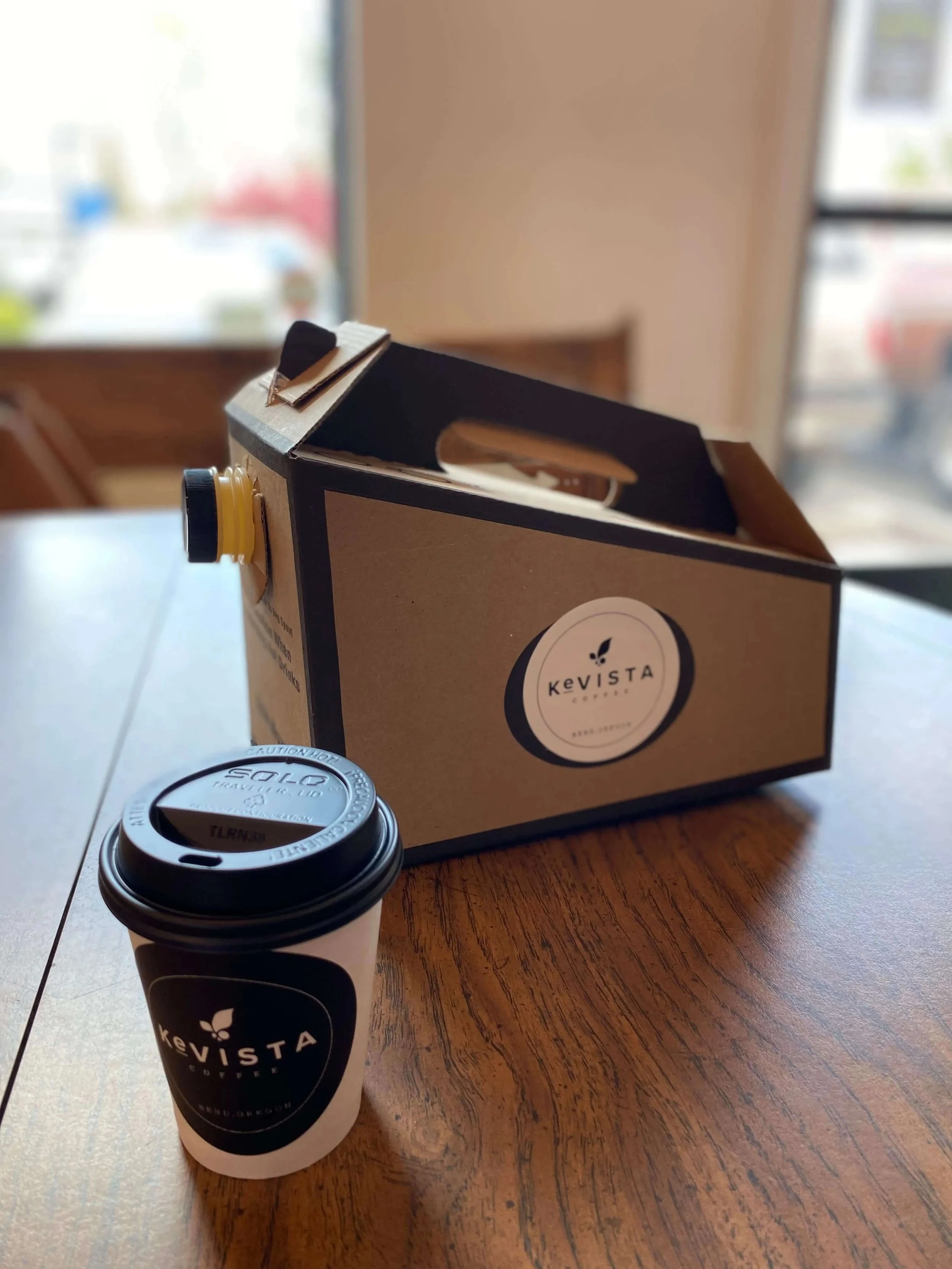 Coffee cup and box with Kevista branding on a wooden table.