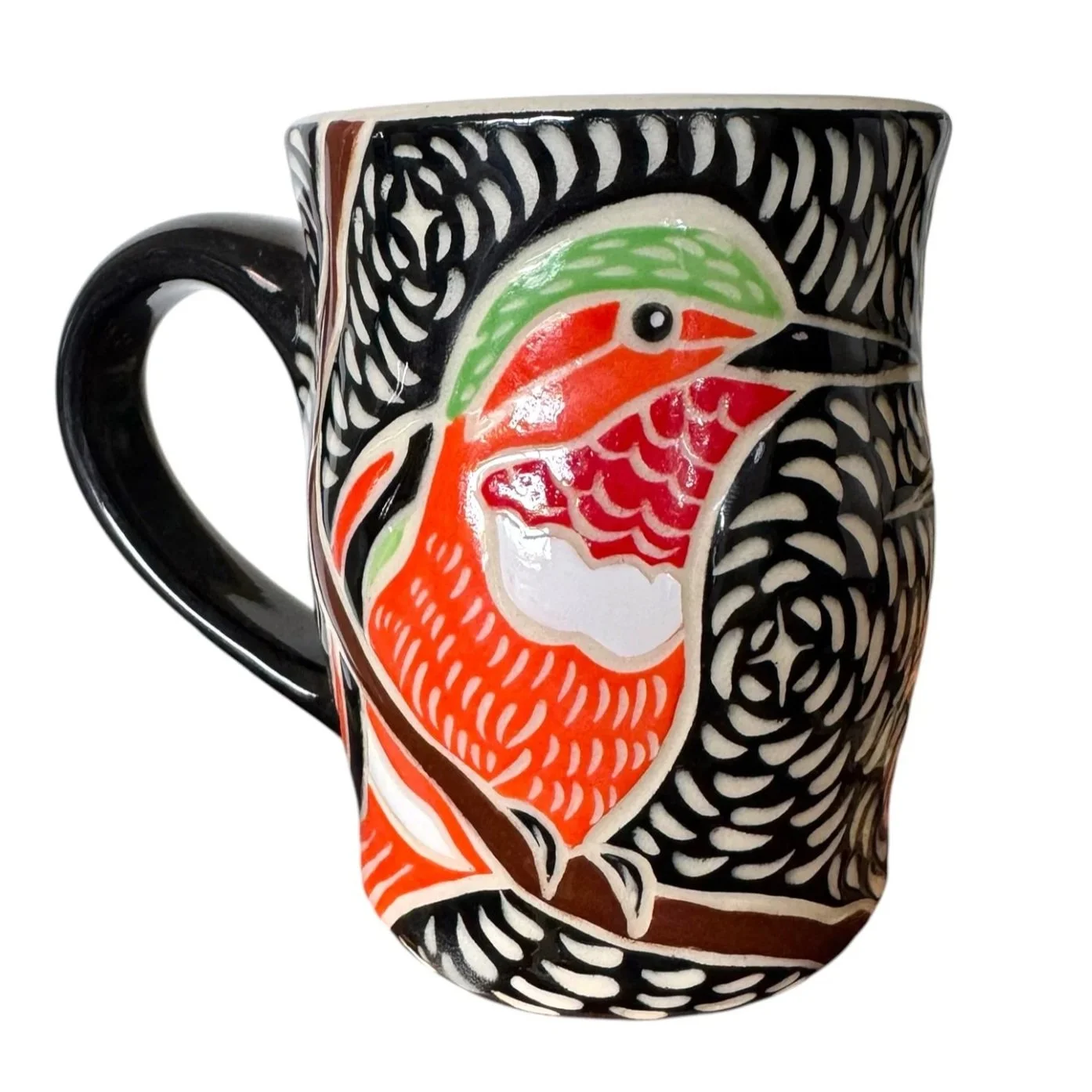 Decorative ceramic mug featuring a colorful, stylized design of a bird with an orange body, green head, and black beak, set against a black and white patterned background.