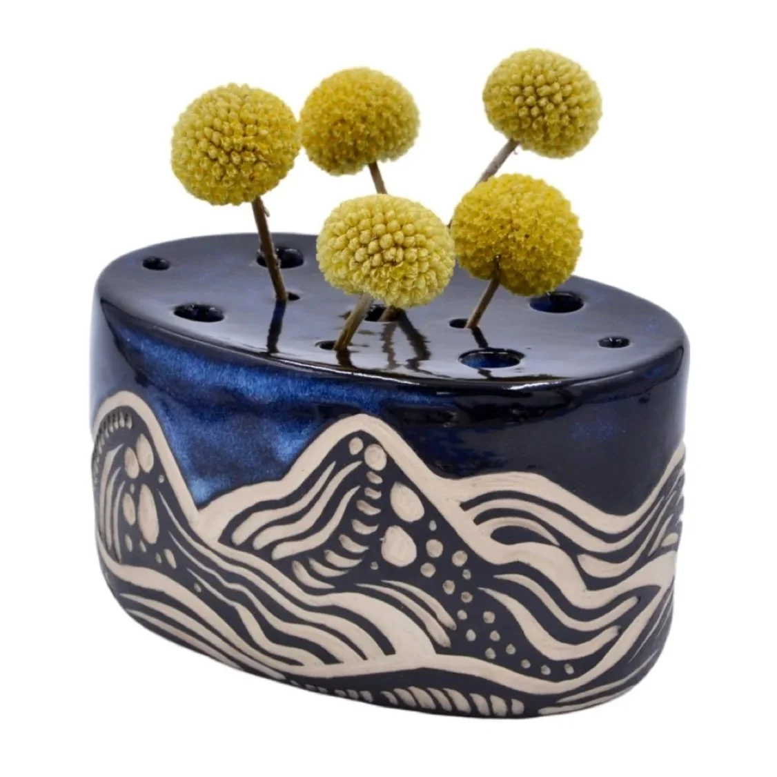 A black ceramic vase with white wave patterns, holding six yellow billy ball flowers with thin stems.