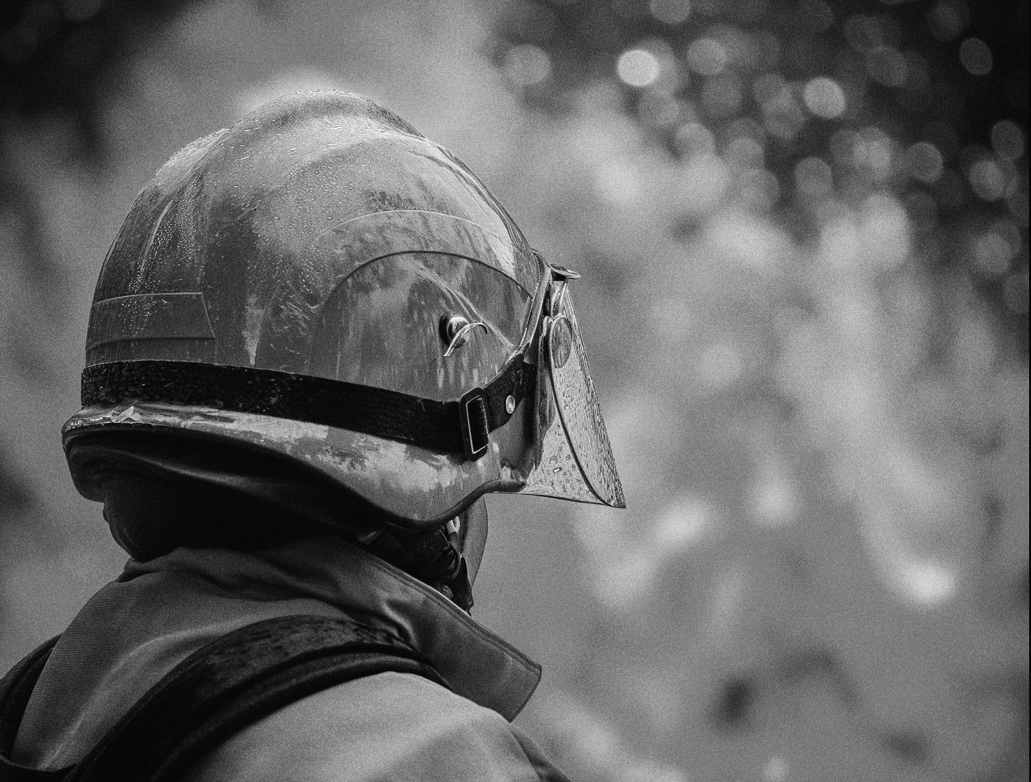 A person wearing a motorcycle helmet with a clear visor and a waterproof jacket. The helmet has droplets of water on it, indicating recent rain or wet conditions.