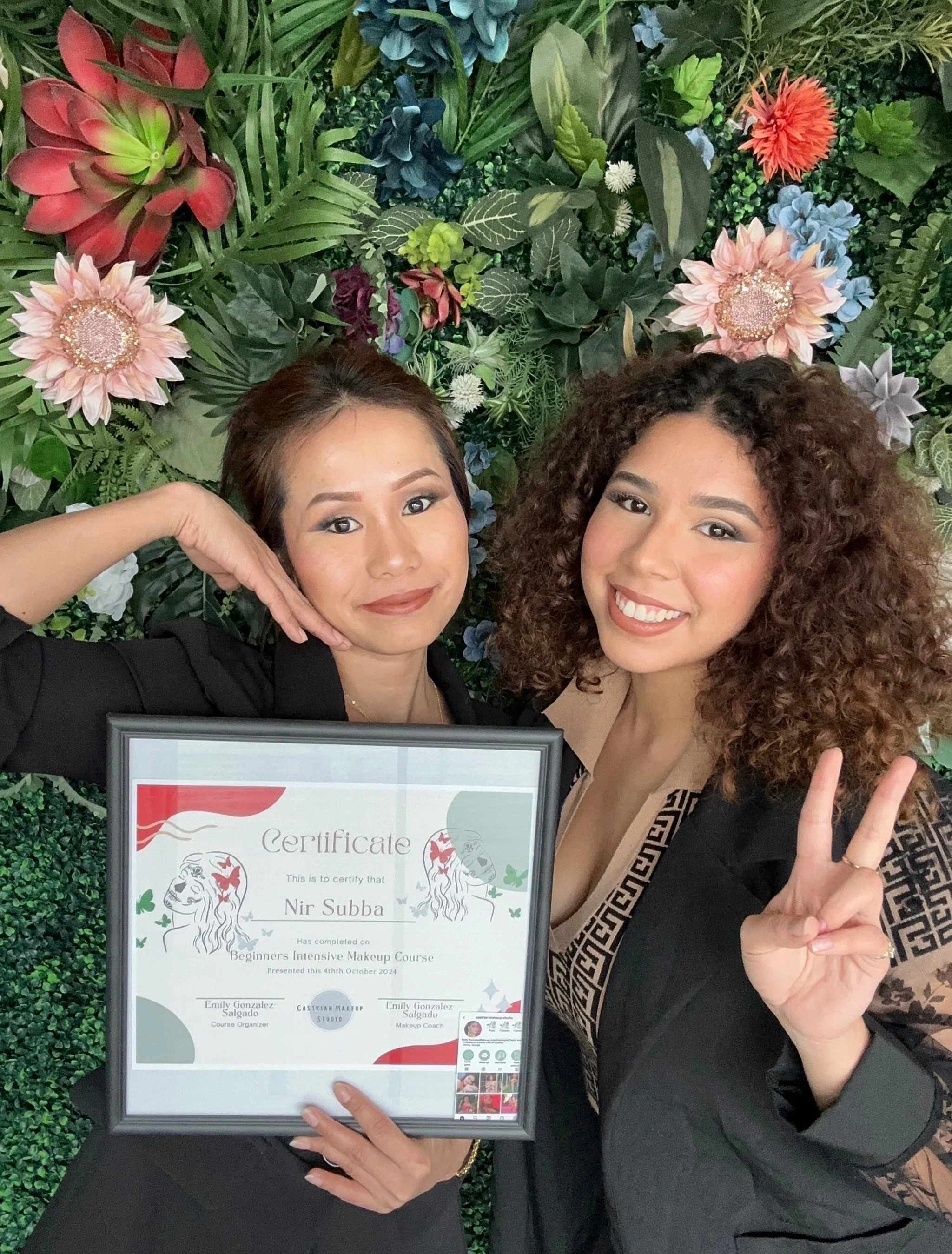 Two women smiling, one holding a framed certificate, standing against a lush green floral backdrop 
Castrian Makeup Studio; Emily Gonzalez; Atlanta, Georgia; Bridal Make-Up; Norcross, Spanish Make-Up Artist; make-up master class