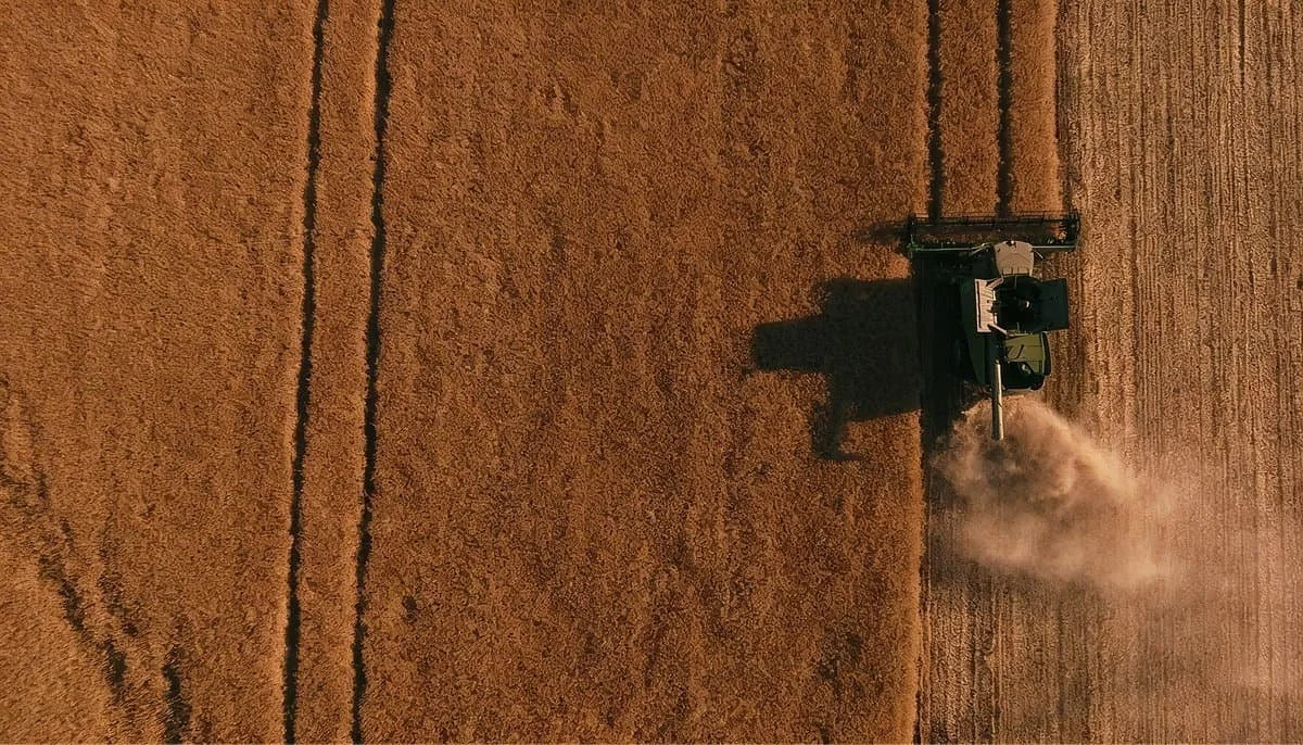 Equipo agrícola robótico autónomo cosechando en un campo, con un dron sobrevolándolo y paneles solares al fondo.