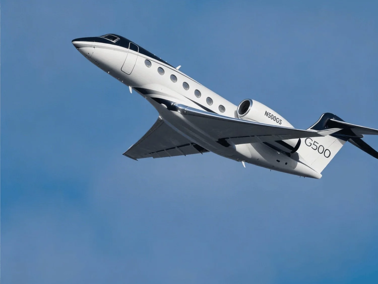 A white and black Gulfstream G500 jet flies upward against a blue sky.