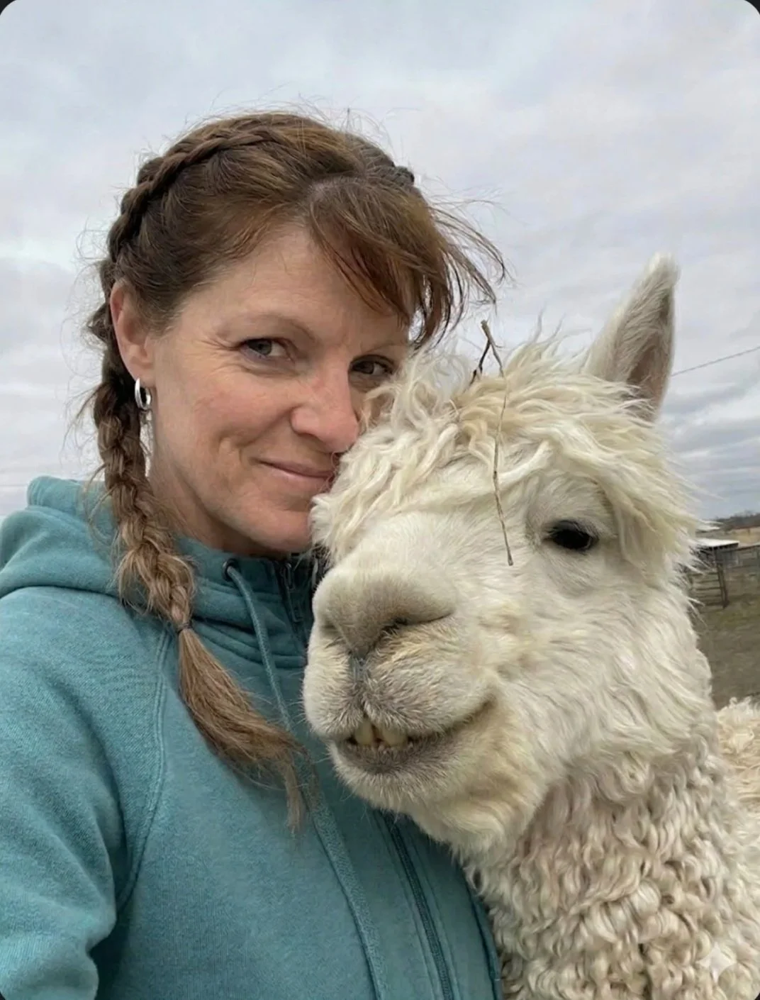 Jana smiling in a close-up moment with an alpaca on the farm