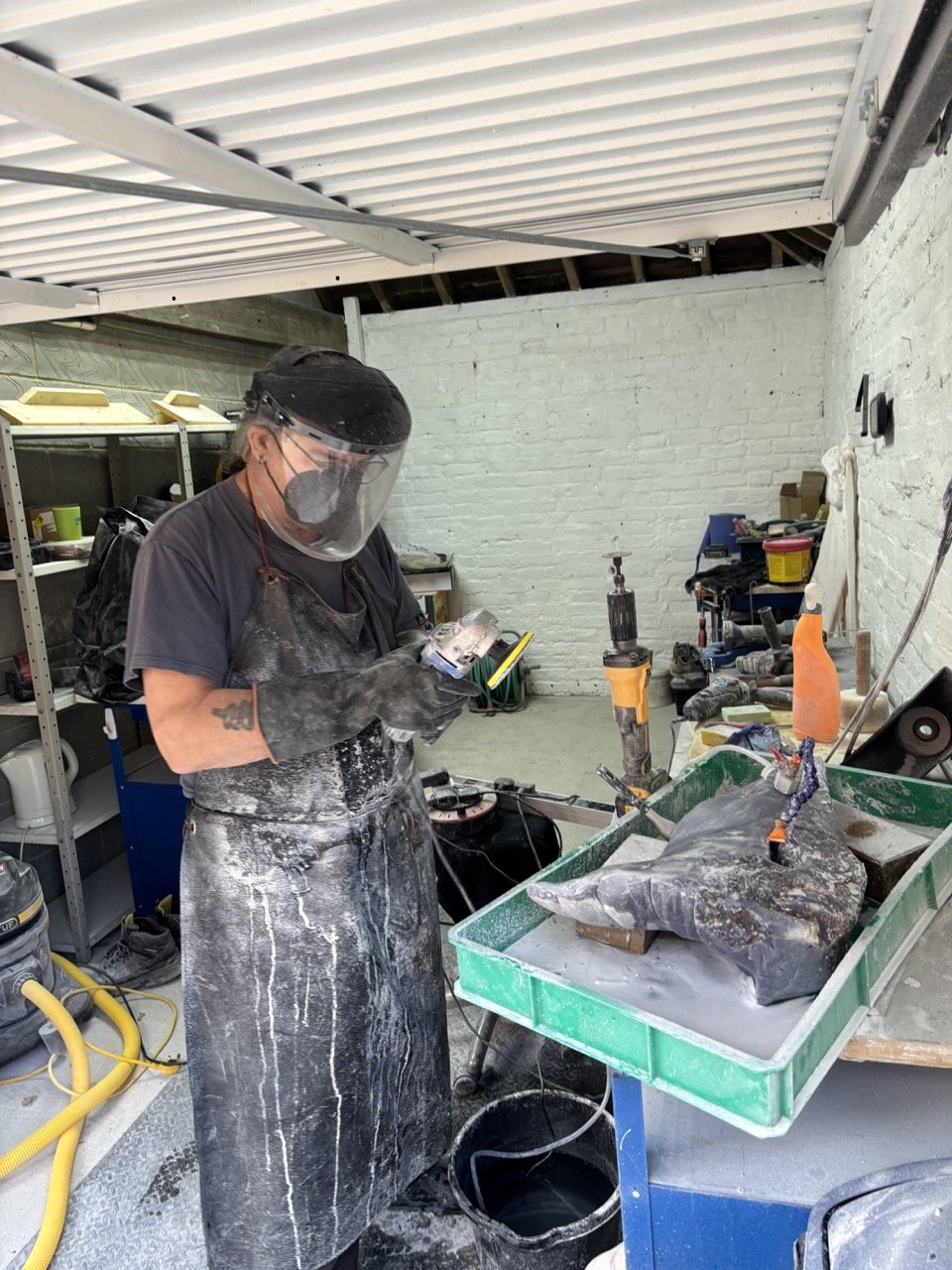 A person in safety gear working in a workshop, handling a chisel and a statue or sculpture on a work table.