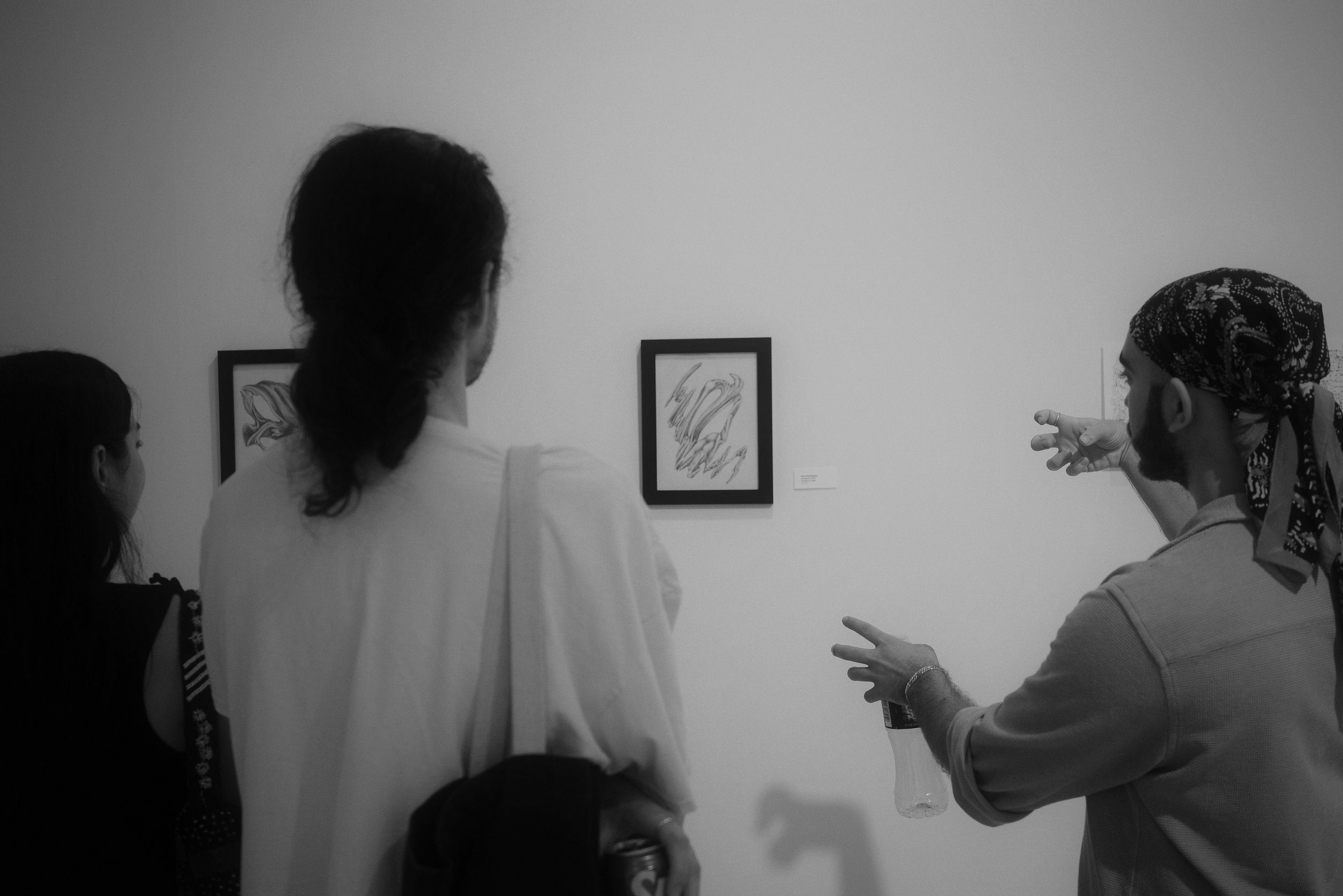 People viewing artwork in a gallery, with one person explaining or presenting, in black and white.