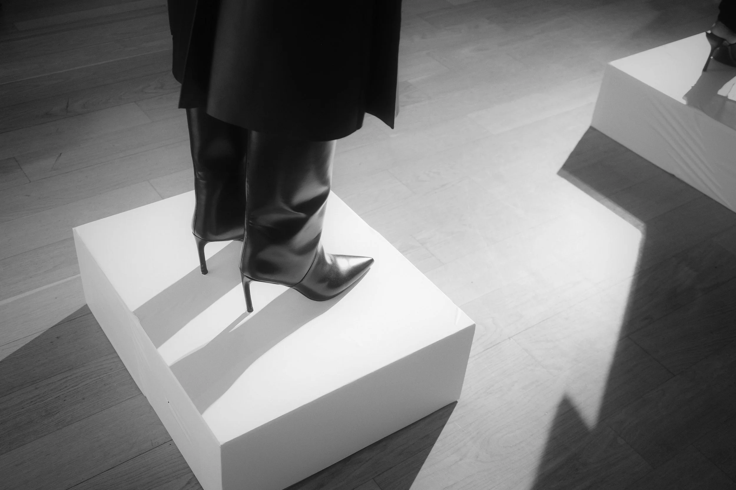 Black high-heeled leather boots on a white display pedestal in an art gallery