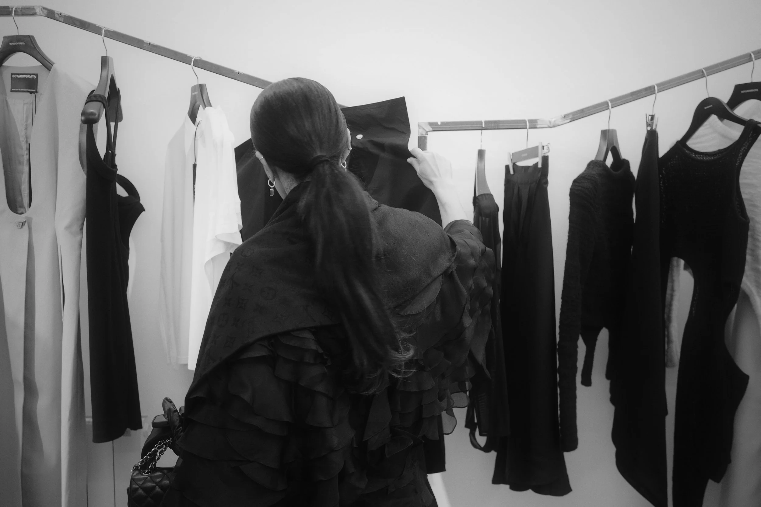 Woman with long hair in a ponytail looking at black and white clothes hanging on a rack.