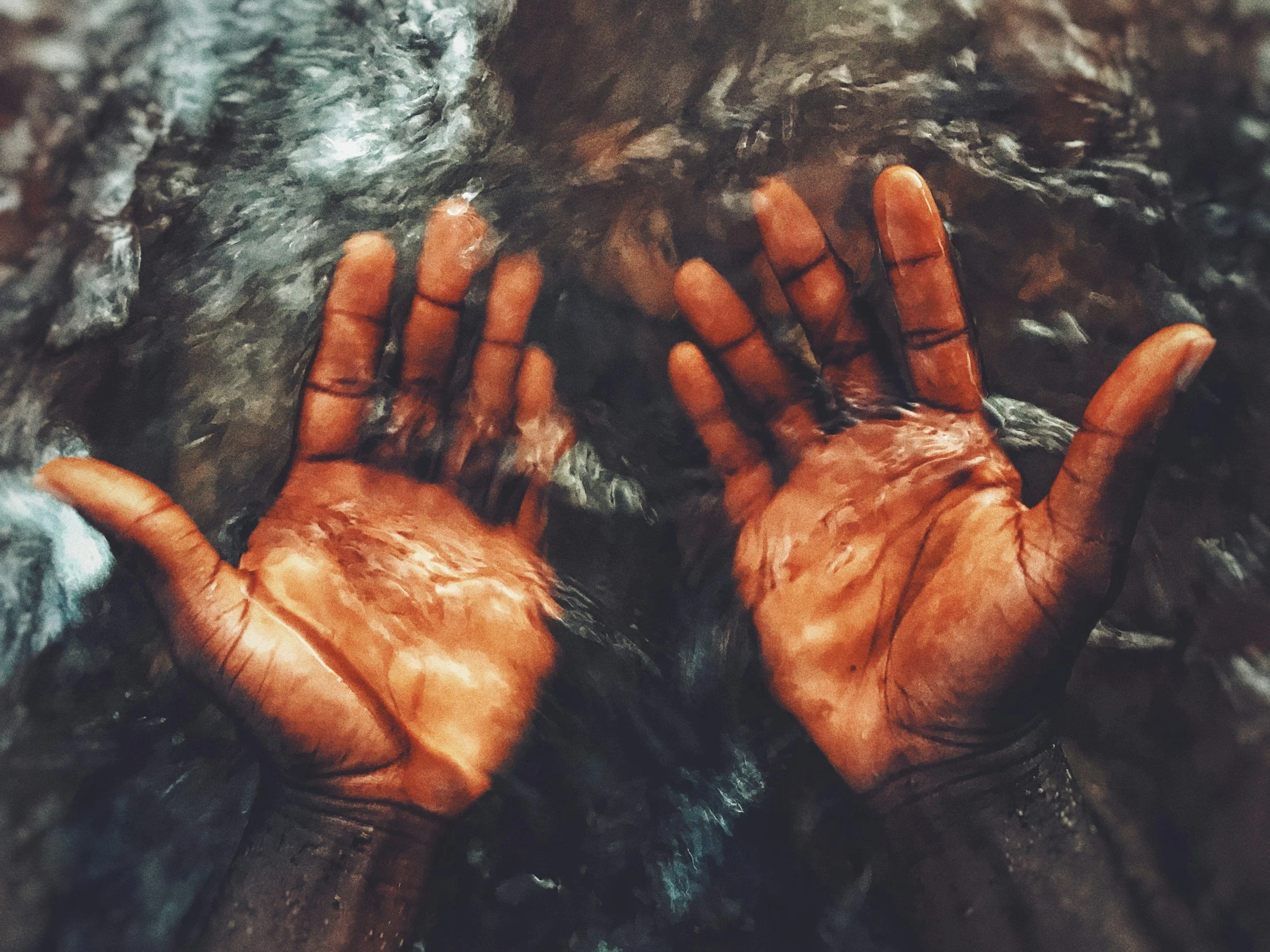 Two hands submerged in water, pressing against a rocky surface.