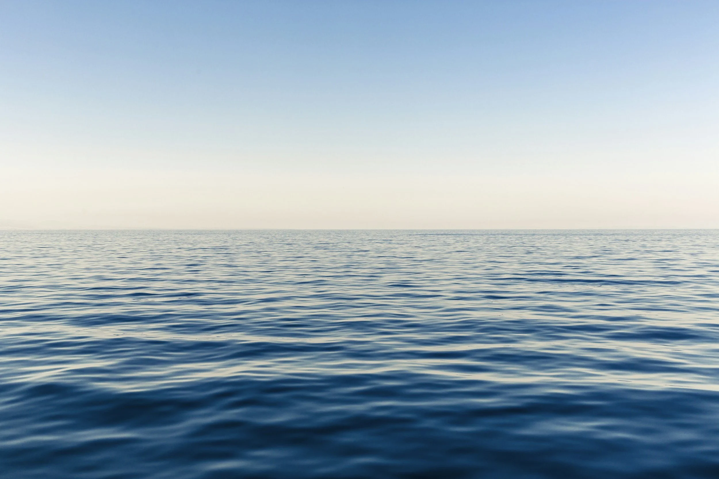 Wide view of calm ocean water with slight ripples, clear sky with no clouds, horizon line in the distance.