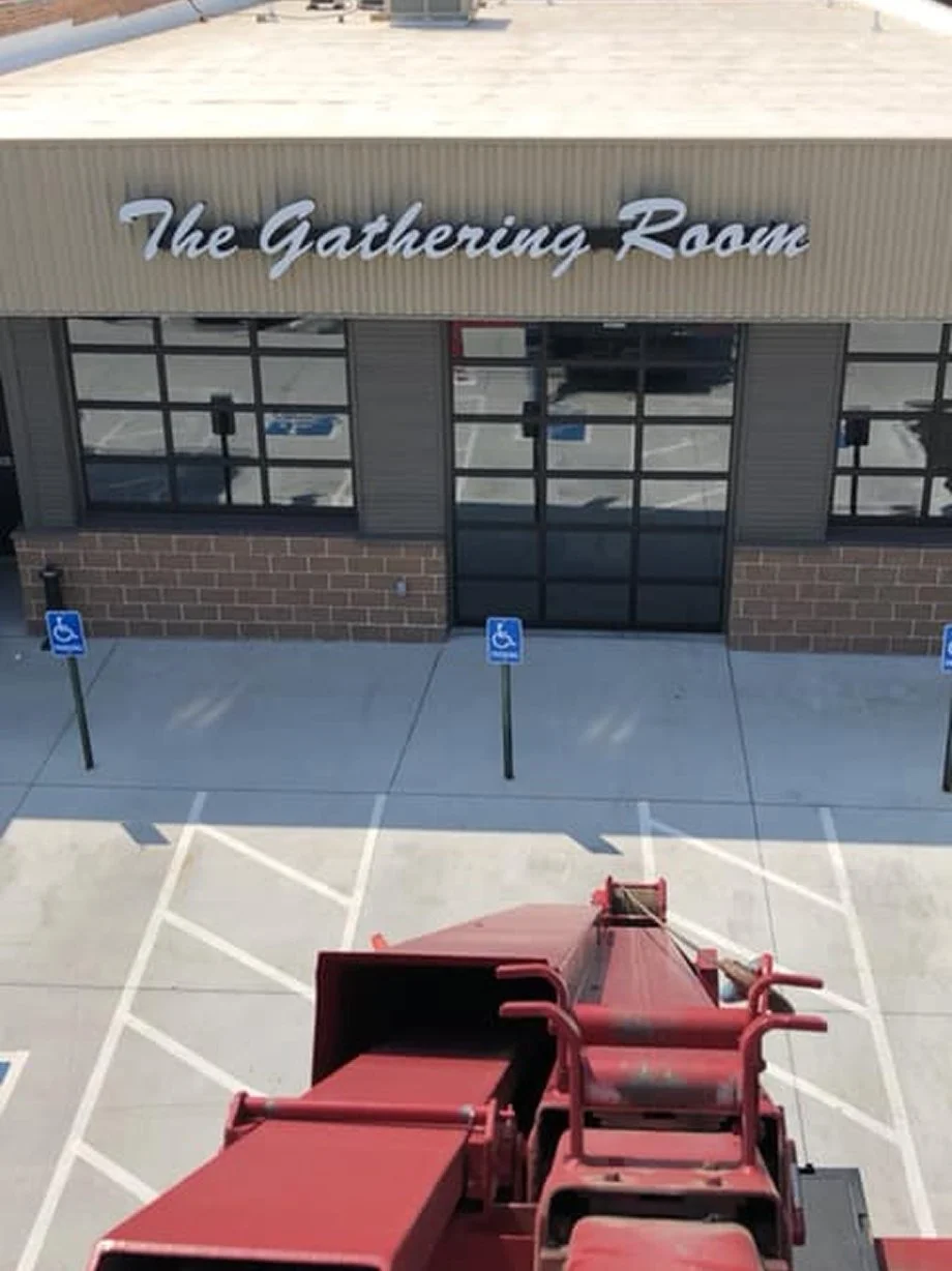 A red semi-truck in a parking lot in front of a building named 'The Gathering Room' with designated handicap parking spots.