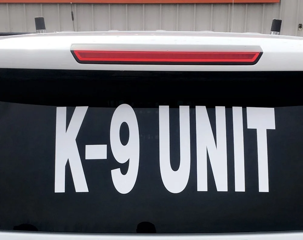 Close-up of the rear window of a police vehicle with a decal reading 'K-9 UNIT' in large white letters.