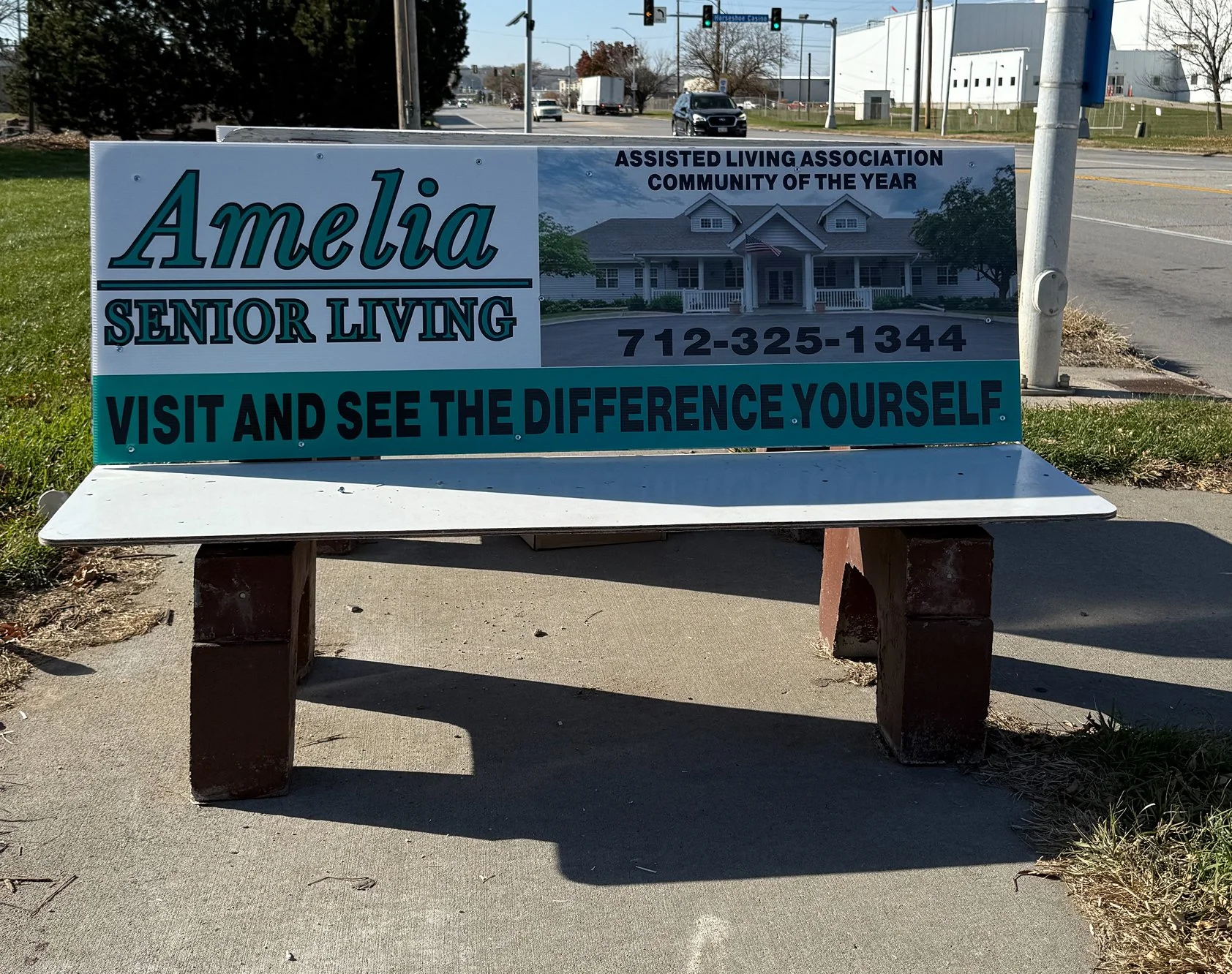 Signboard advertising Amelia Senior Living, an assisted living community, with the phone number 712-325-1344 and the slogan 'Visit and see the difference yourself'.