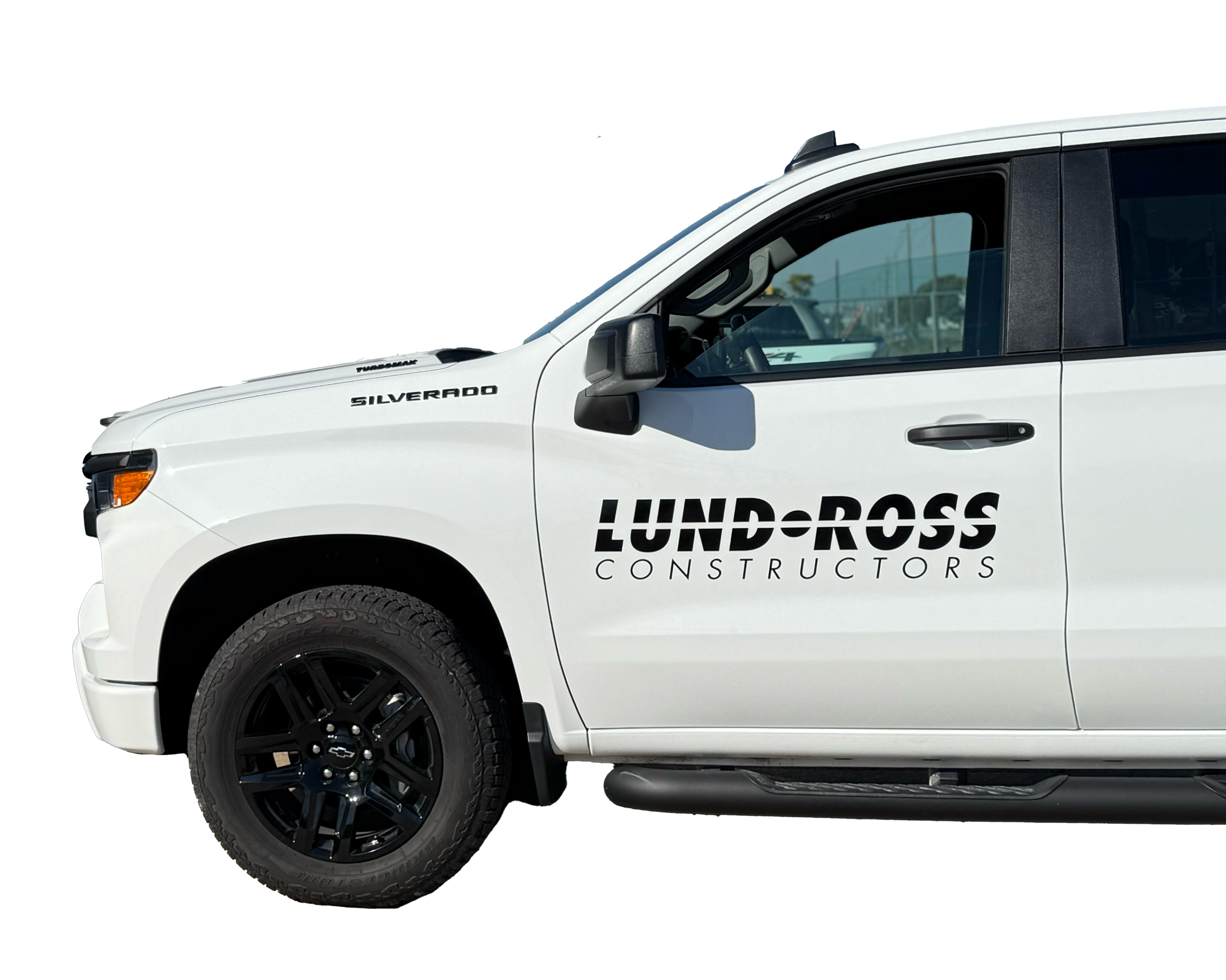 White Chevrolet Silverado truck with black wheels, with the logo 'Lundross Constructors' on the door.
