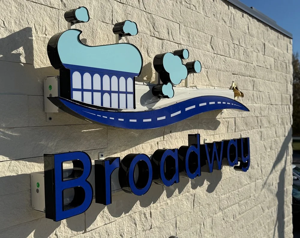 Sign with a cupcake graphic and the word "Broadway" on a brick wall.
