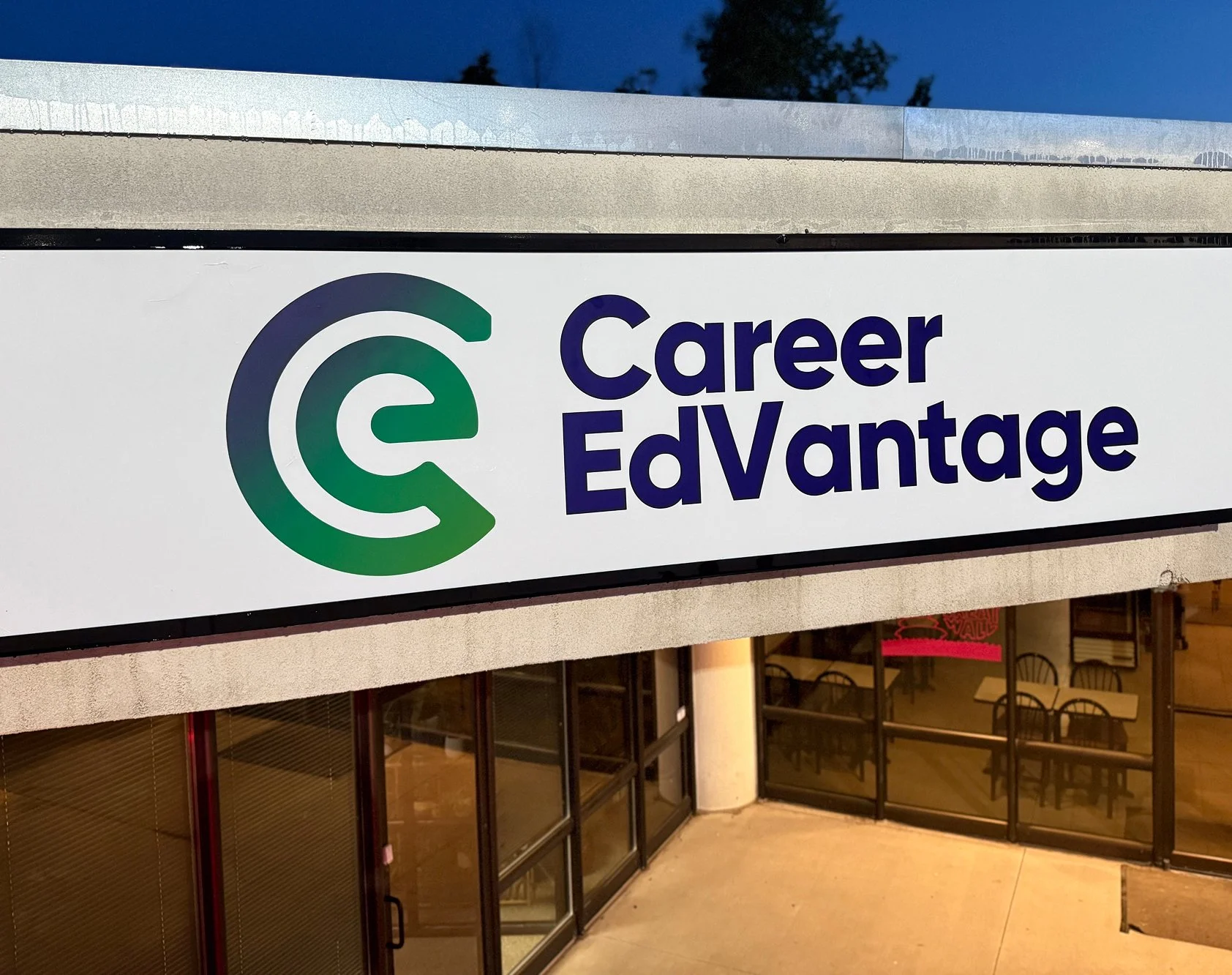 Sign for Career EdVantage outside a building, with an interior view of tables and chairs visible through glass doors.
