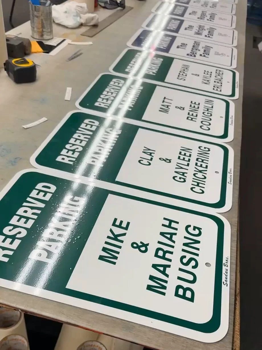 A series of green and white reserved parking signs with names of family members and their vehicles arranged on a worktable.