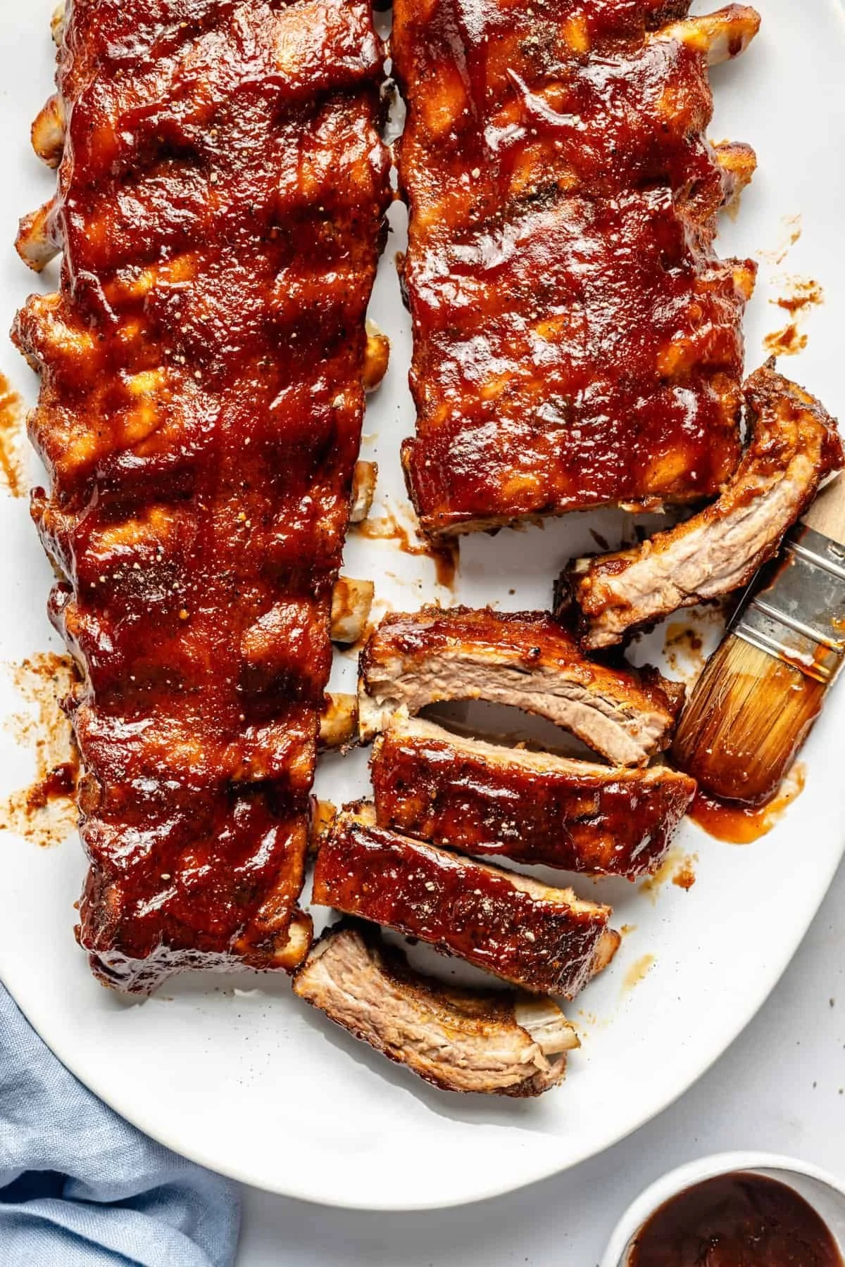 Barbecue pork ribs on a white platter, with some ribs cut into pieces and small bowls of barbecue sauce nearby.
