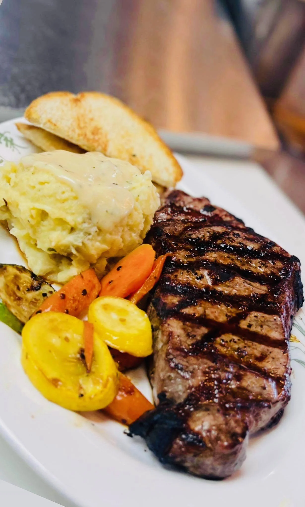Grilled steak with grilled vegetables, mashed potatoes with gravy, a slice of bread, and roasted zucchini.