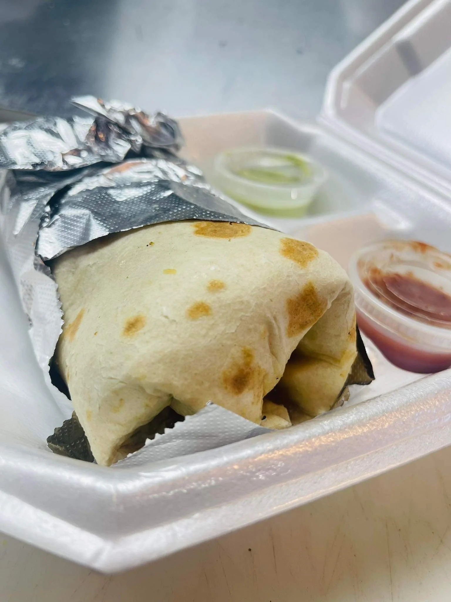 A partially unwrapped burrito with condiments in a foam takeout box.