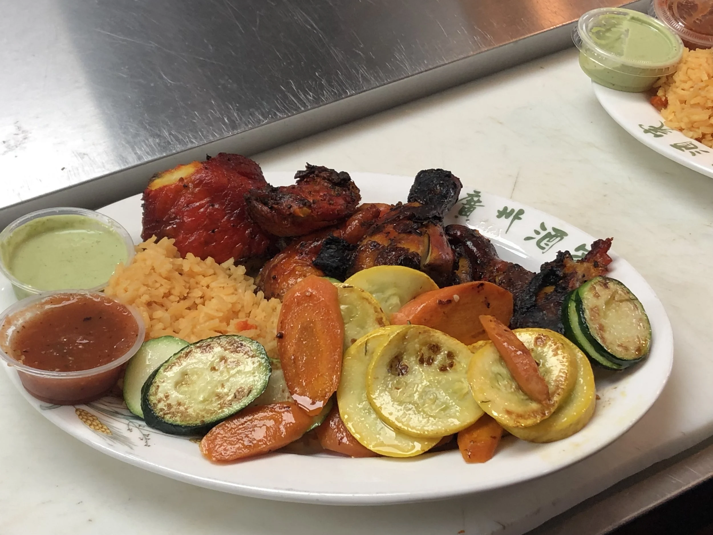 Plate of grilled chicken with vegetables, rice, and sauces on a white oval plate