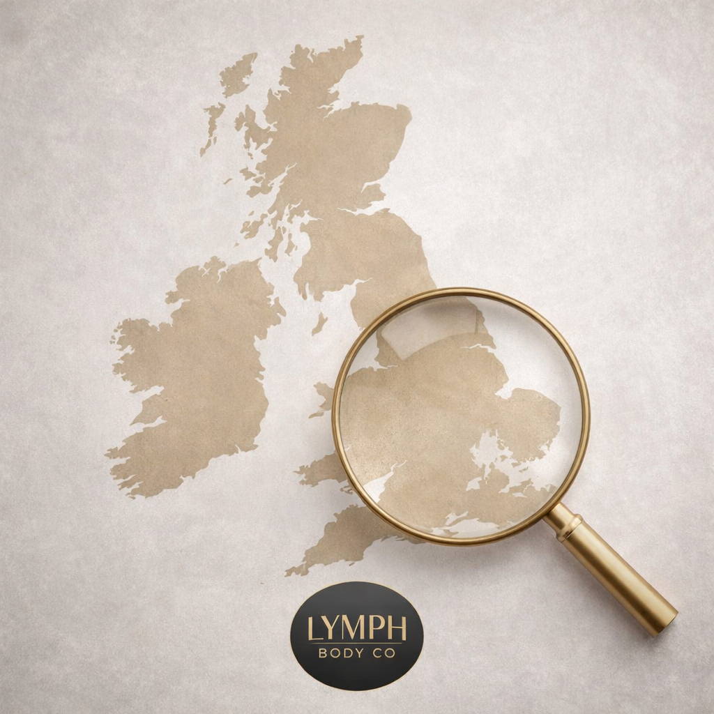 A beige map of Europe on a white surface with a gold magnifying glass over Greece. There is a black circular logo with gold text reading 'LYMPH BODY CO' at the bottom of the image.