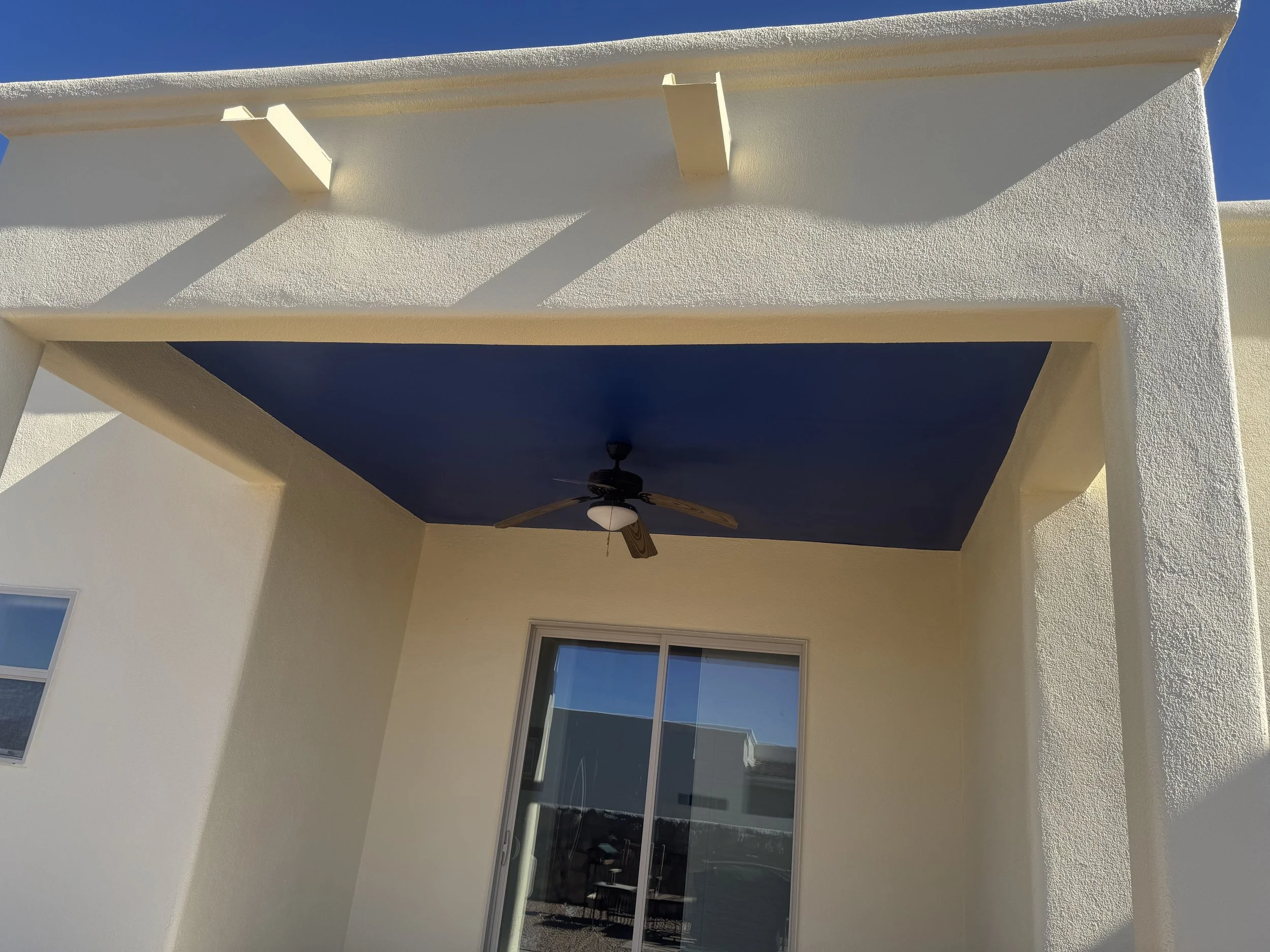 Exterior view of a white building with a screened porch area with a ceiling fan, partially visible windows, and a clear blue sky above.