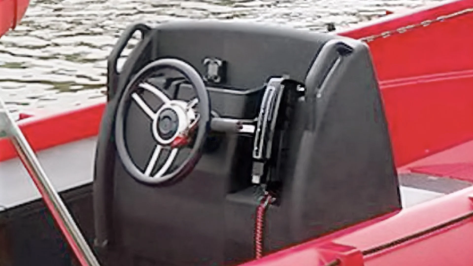 Close-up of a black steering wheel and dashboard in a red boat, with water in the background.