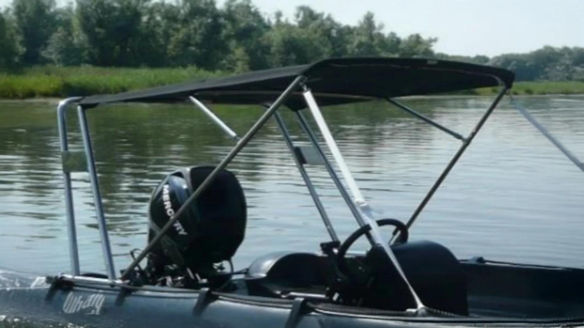 A small motorboat cruising on a calm river with green trees on the riverbank in the background.