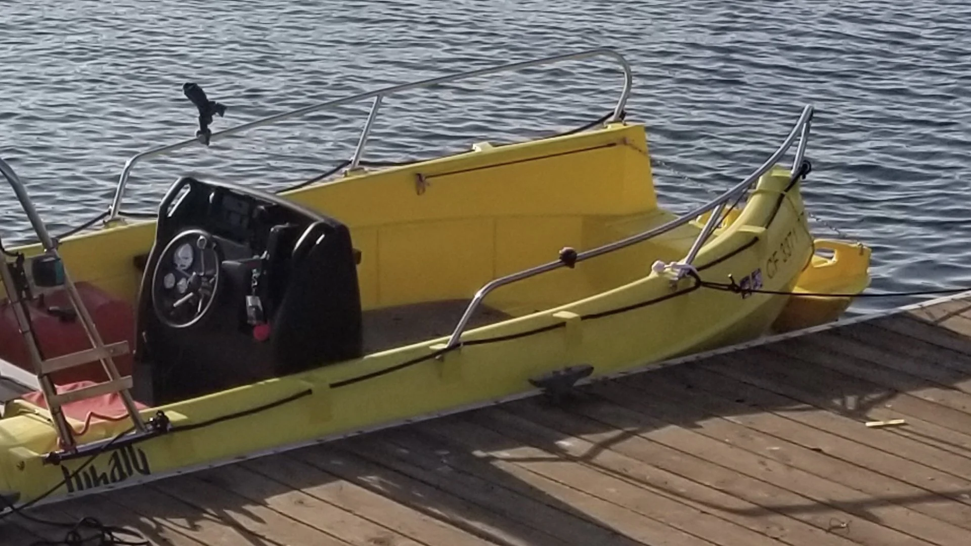 Yellow motorboat docked at a wooden pier on a body of water, with the boat's interior and steering console visible.