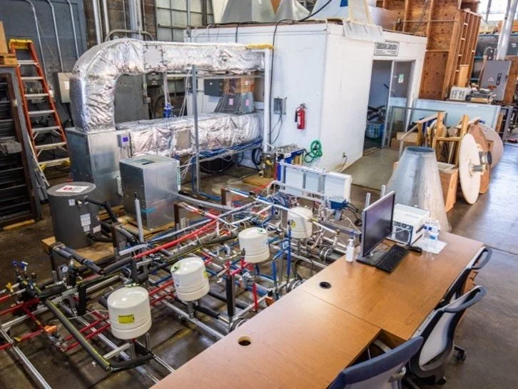 Industrial laboratory with pipes, tanks, and computer setup.