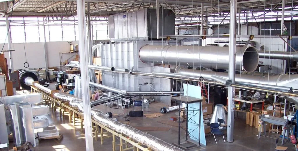 Industrial workshop with large ventilation ducts, equipment, and tools.